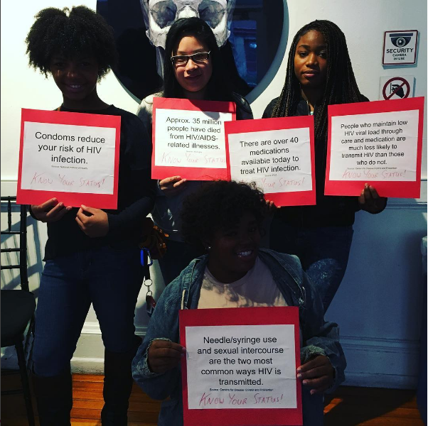 Four students in the Teva Pharmaceuticals Internship pose with signs displaying various facts about HIV/AIDS at World AIDS Day 2016